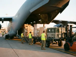 Grote vrachtvliegtuig met open laadruim waar pallets met pakketten worden geladen door grondpersoneel op luchthaven