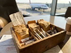 Houten kist met gelabelde zadenpakketten en glazen flesjes op luchthaventafel, vliegtuig op achtergrond
